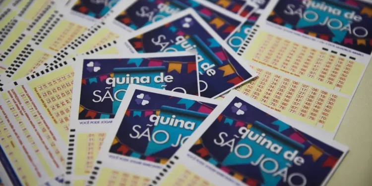 Cartelas da Quina de São João 2025 espalhadas sobre a mesa, com destaque para números da sorte e banners coloridos.