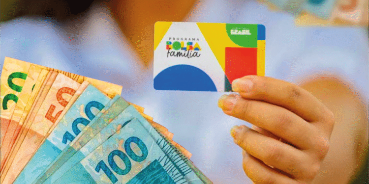 Pessoa segurando cartão do Bolsa Família ao lado de notas de dinheiro.
