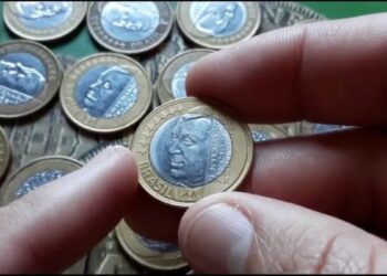 Pessoa segurando moeda comemorativa de R$1 do Juscelino Kubitschek de 2002 em destaque