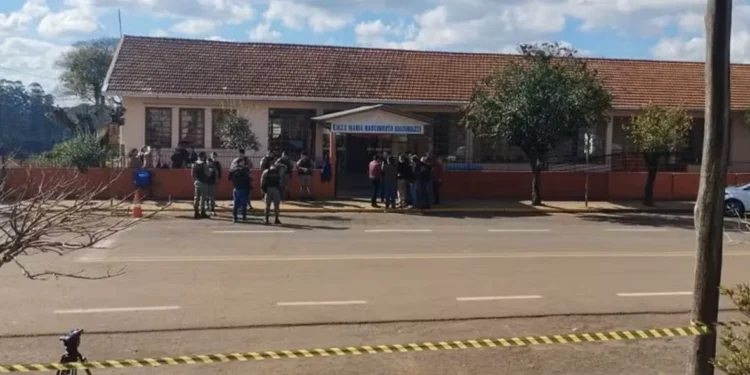 Imagem da escola Maria Nascimento Giacomazzi com a presença de policiais em frente, com cordão de isolamento e investigação em andamento.