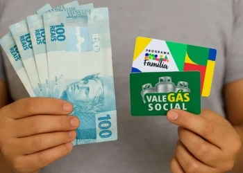 Pessoa segura notas de 100 reais e cartões do Bolsa Família e Vale Gás Social.