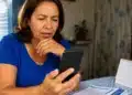 Mulher consultando informações sobre o benefício do INSS pelo celular, representando a verificação da data de pagamento do INSS de julho para beneficiários que recebem acima de um salário mínimo.