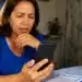 Mulher consultando informações sobre o benefício do INSS pelo celular, representando a verificação da data de pagamento do INSS de julho para beneficiários que recebem acima de um salário mínimo.
