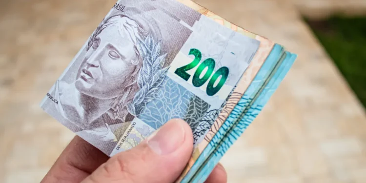 Pessoa segurando várias cédulas de 200 reais, simbolizando pagamento em dinheiro.