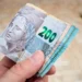 Pessoa segurando várias cédulas de 200 reais, simbolizando pagamento em dinheiro.