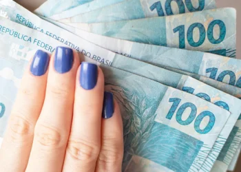 Mão feminina segurando cédulas de 100 reais.