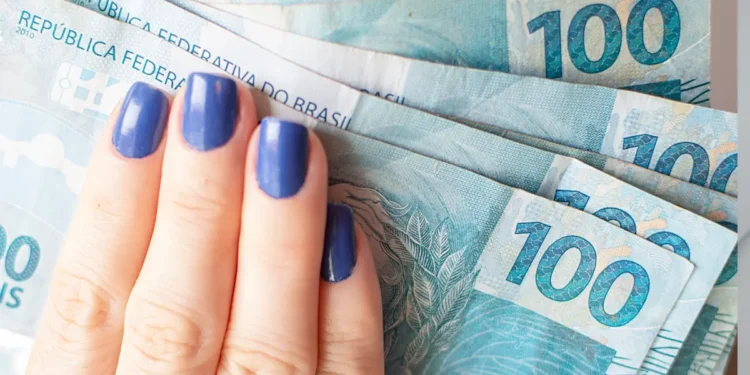 Mão feminina segurando cédulas de 100 reais.