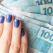Mão feminina segurando cédulas de 100 reais.