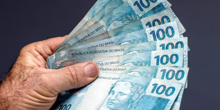 Notas de 100 reais sendo seguradas por uma mão.