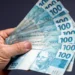 Notas de 100 reais sendo seguradas por uma mão.