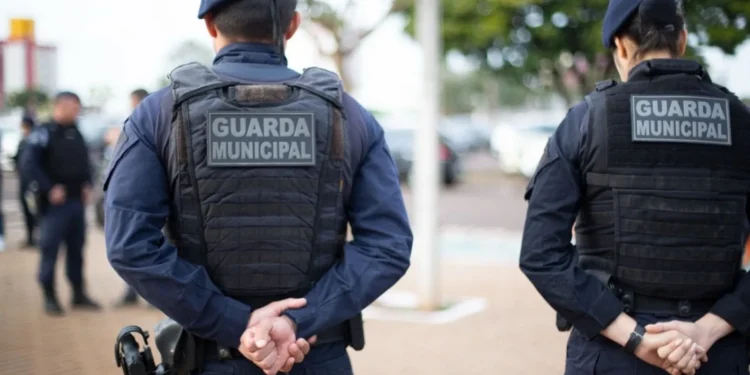 Dois agentes da Guarda Municipal de costas em patrulhamento urbano.