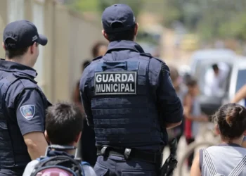 Guardas Municipais de costas em patrulhamento com presença da comunidade.