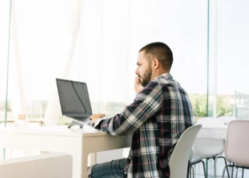 Homem trabalhando no computador e falando ao telefone, simbolizando a análise de concursos públicos.