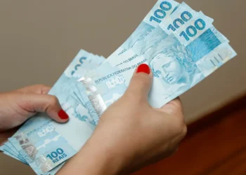Mão de estudante segurando notas de 100 reais