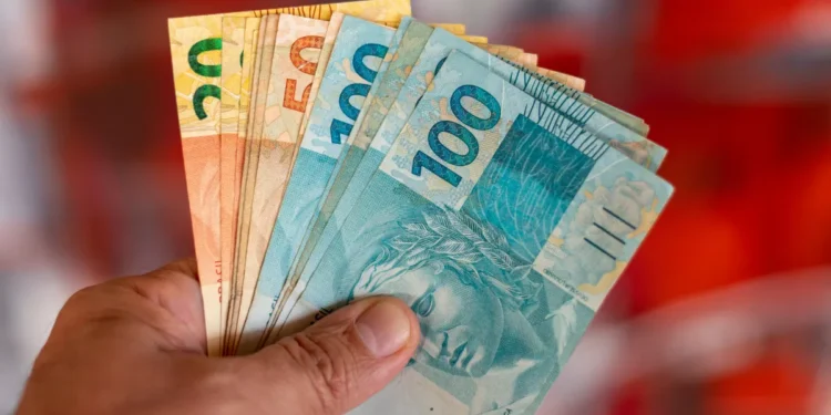 Pessoa segurando notas de reais de diferentes valores.