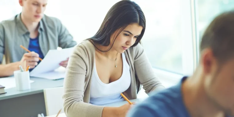Estudantes em sala de prova respondendo questões de forma concentrada.
