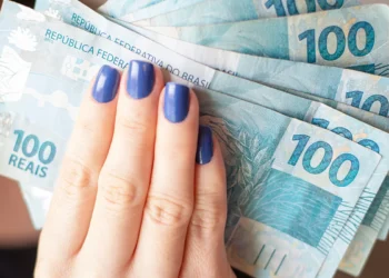 Notas de 100 reais sendo seguradas por uma mão com unhas pintadas