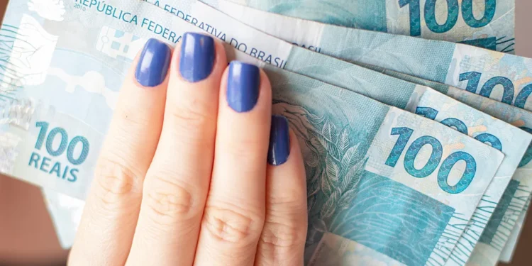 Notas de 100 reais sendo seguradas por uma mão com unhas pintadas