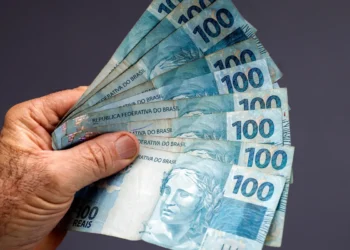 Pessoa segurando notas de R$ 100 que simbolizam o pagamento do abono salarial do PIS/Pasep.