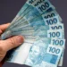 Pessoa segurando notas de R$ 100 que simbolizam o pagamento do abono salarial do PIS/Pasep.