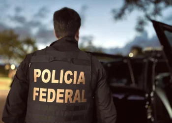 Agente da Polícia Federal de costas durante operação ao anoitecer.