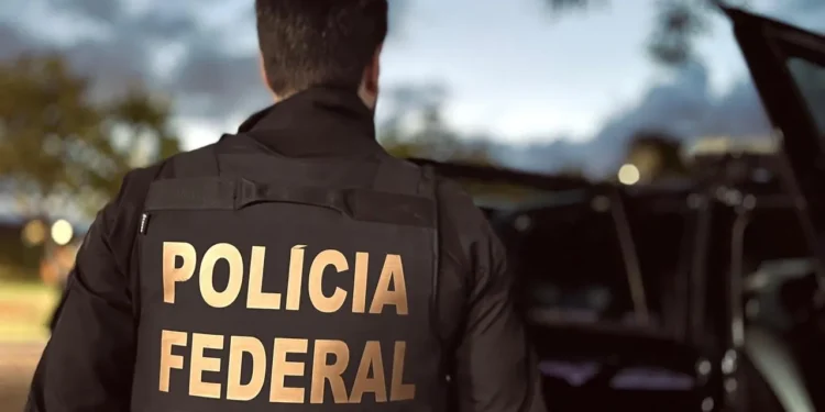 Agente da Polícia Federal de costas durante operação ao anoitecer.