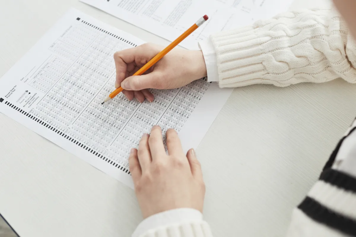 Pessoa preenchendo gabarito de prova com lápis.