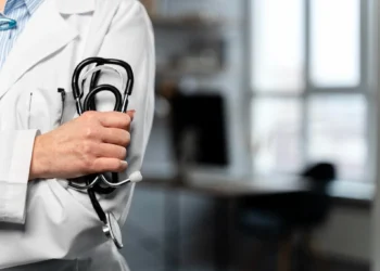 Profissional da saúde com jaleco branco segurando estetoscópio.