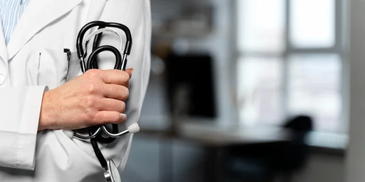 Profissional da saúde com jaleco branco segurando estetoscópio.