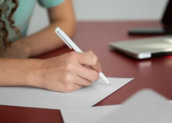 Mão escrevendo em uma folha de papel com caneta branca, simbolizando a redação do Encceja.