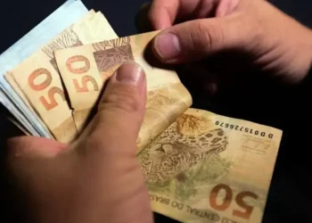 Mão segurando cédulas de R$100 e logo do FGTS, simbolizando o saque dos valores distribuídos.