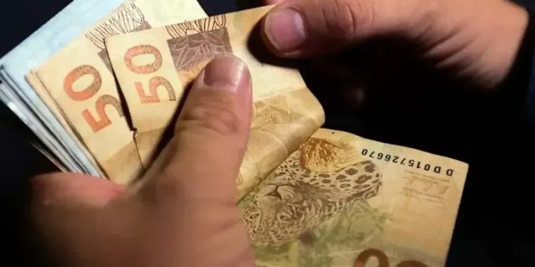 Mão contando cédulas de R$ 50, simbolizando o depósito do FGTS para trabalhadores CLT.