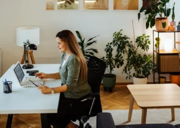 Mulher concentrada no computador trabalhando de casa em um ambiente moderno e organizado.