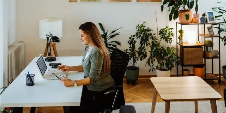 Mulher concentrada no computador trabalhando de casa em um ambiente moderno e organizado.