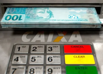Notas de R$ 100 sendo retiradas de um caixa eletrônico da CAIXA Econômica Federal com saldo disponível de R$ 708.