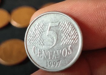 Close-up de uma moeda de 5 centavos do ano de 1997 sendo segurada com os dedos.