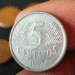 Close-up de uma moeda de 5 centavos do ano de 1997 sendo segurada com os dedos.