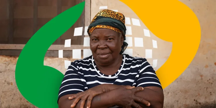 Mulher idosa com camiseta listrada e lenço na cabeça, com os braços cruzados, em frente a uma parede de cimento com elementos gráficos coloridos ao fundo.