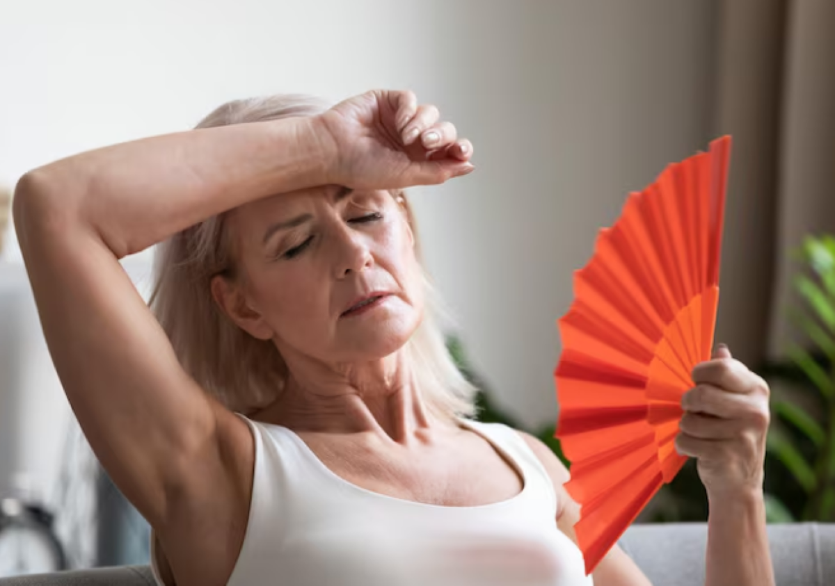 Sintomas da Menopausa: O Início do Climatério Mulher de meia-idade se abanando com leque, sentindo as ondas de calor da menopausa