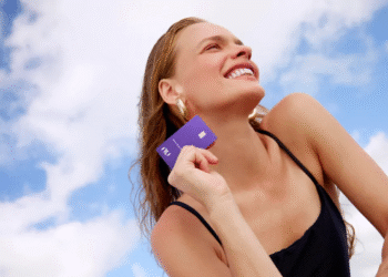 Mulher sorrindo ao segurar o cartão Ultravioleta da Nubank sob o céu azul.