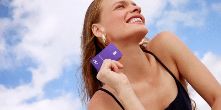 Mulher sorrindo ao segurar o cartão Ultravioleta da Nubank sob o céu azul.