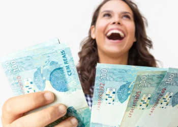 Pessoa sorrindo enquanto segura notas de R$ 100, representando um pagamento extra.