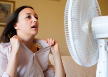Mulher com sintomas de menopausa se refrescando com ventilador