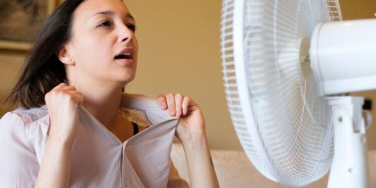 Mulher com sintomas de menopausa se refrescando com ventilador