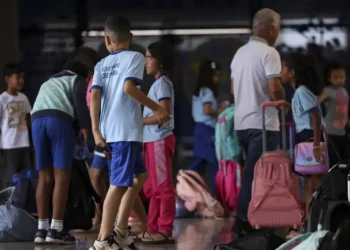 Alunos chegam à escola com mochilas e materiais escolares.