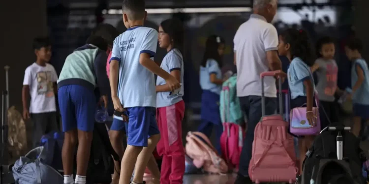 Alunos chegam à escola com mochilas e materiais escolares.