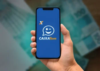 Aplicativo Caixa Tem aberto na tela do celular com notas de 100 reais ao fundo.