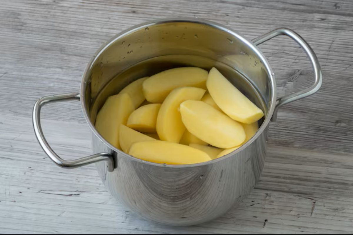 Preparação da batata crua para o truque culinário Batatas descascadas e cortadas dentro de uma panela de inox, preparadas para uso