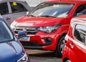 Fiat Mobi vermelho estacionado entre outros carros iluminados pelo sol.