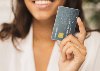 Mulher sorrindo segura cartão de crédito moderno com chip dourado, close nas mãos.